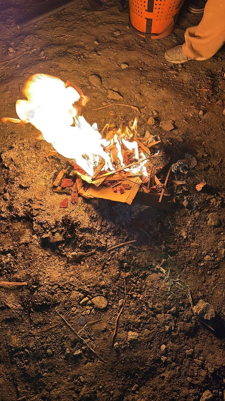 Bonfire of wood and cardboard burning on bare ground at night