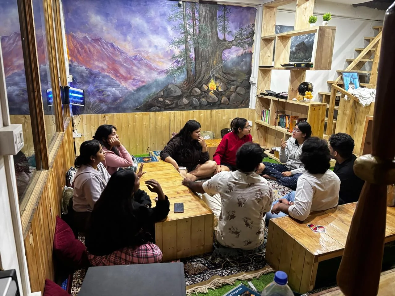 A group of guests talking together in the café beneath a hand-painted mural of a pine tree and campfire in the mountains
