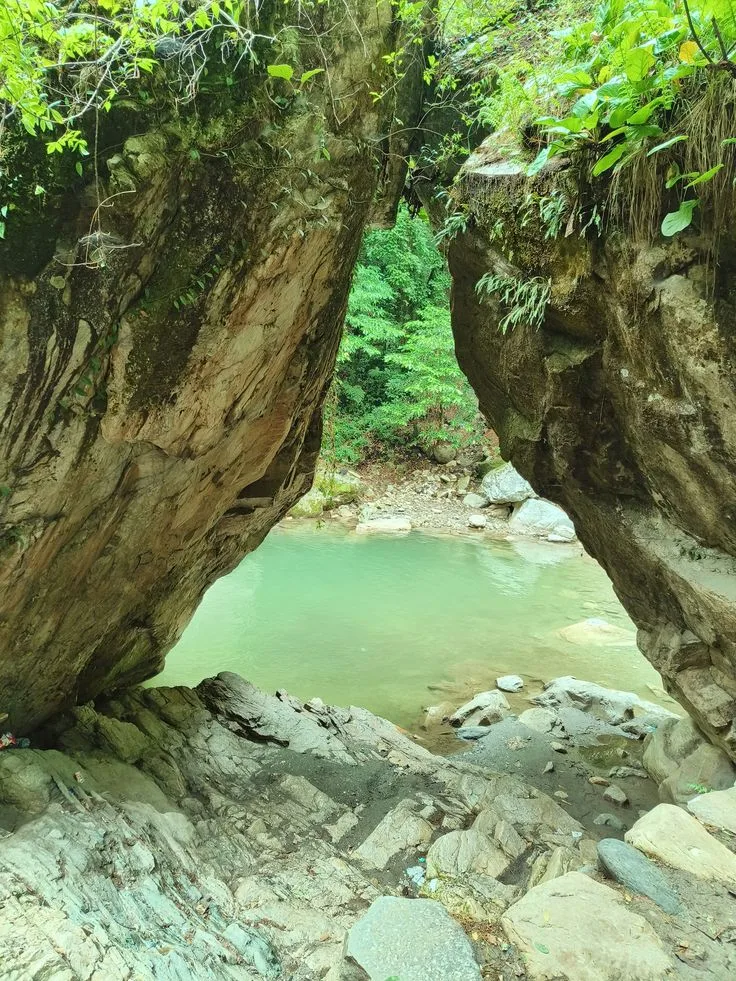 Mini Thailand, a natural rock arch framing a green river pool surrounded by ferns and forest