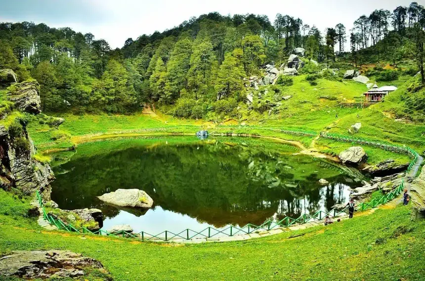 Serolsar Lake, a green mountain lake near Jibhi ringed by pine forest, with a small temple on the hillside