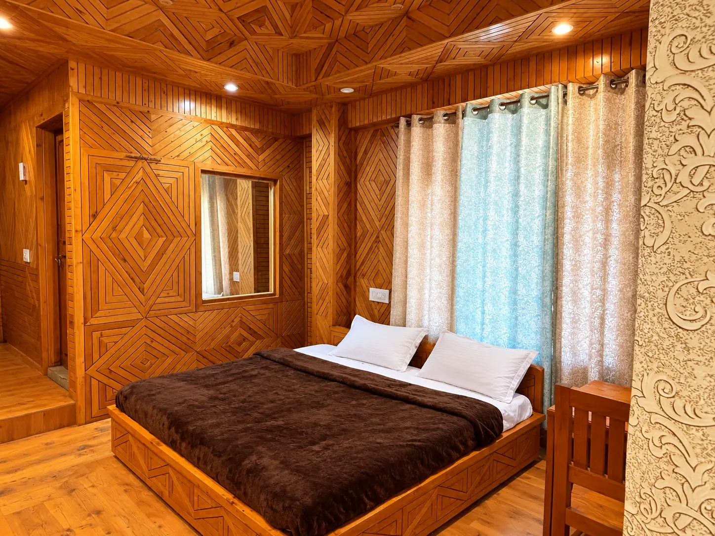 Deluxe Double Room bedroom with diamond-patterned pine wood walls and ceiling, a large bed and curtained windows